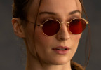 Sophie Turner as Lara Croft wears round sunglasses with red lenses in the series Tomb Raider.
