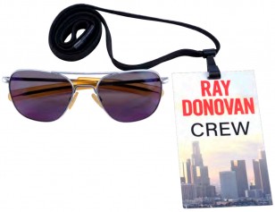 A Prop Store auction in June 2022 offered this screen-used pair of Randolph Engineering Aviator sunglasses in a matte chrome frame with American Gray lenses; a black leather Randolph glasses case hand-labeled “Ray 2 (Purple AR Coat)” with a snap-button closure; and a crew lanyard from the production. The lenses exhibit some scratching from production wear, and the case’s leather is cracking from age.