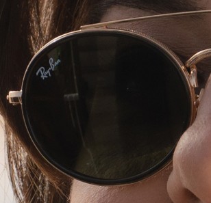 Detail of the sunglasses worn by Aubrey Plaza shows the gold frame wth black edges.